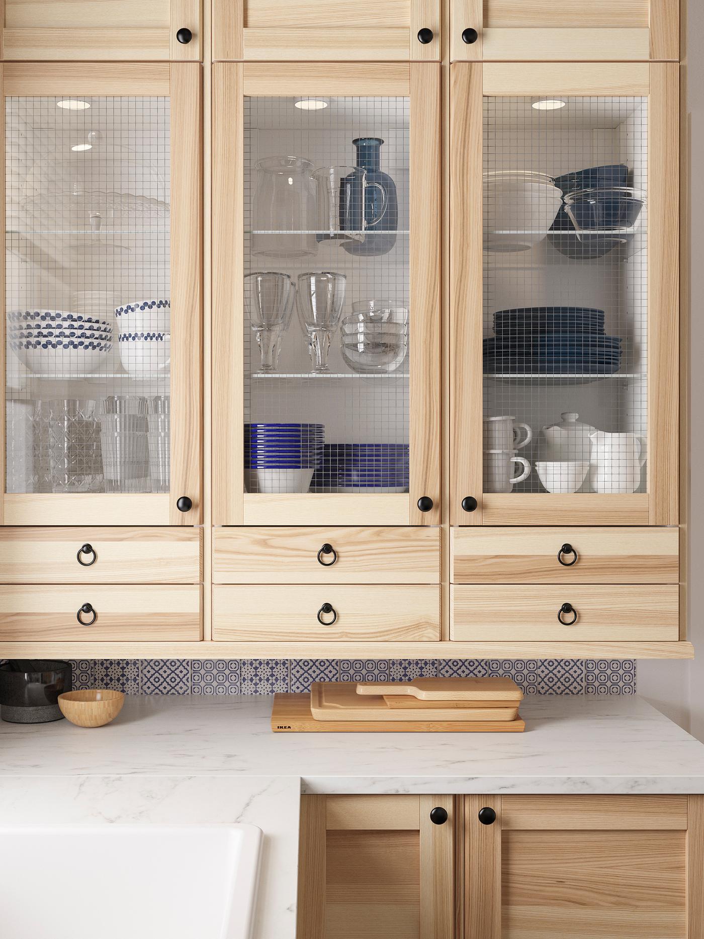 Armoires murales avec portes vitrées en frêne TORHAMN contenant un service de table au-dessus d’un plan de travail à effet marbre blanc.