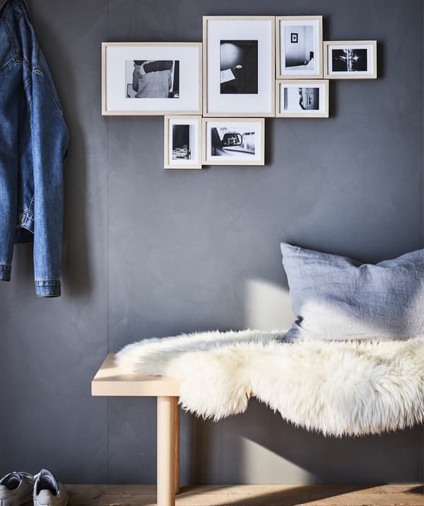 Arrangement de photos en noir et blanc sur un mur gris. En dessous, un banc et une peau de mouton.
