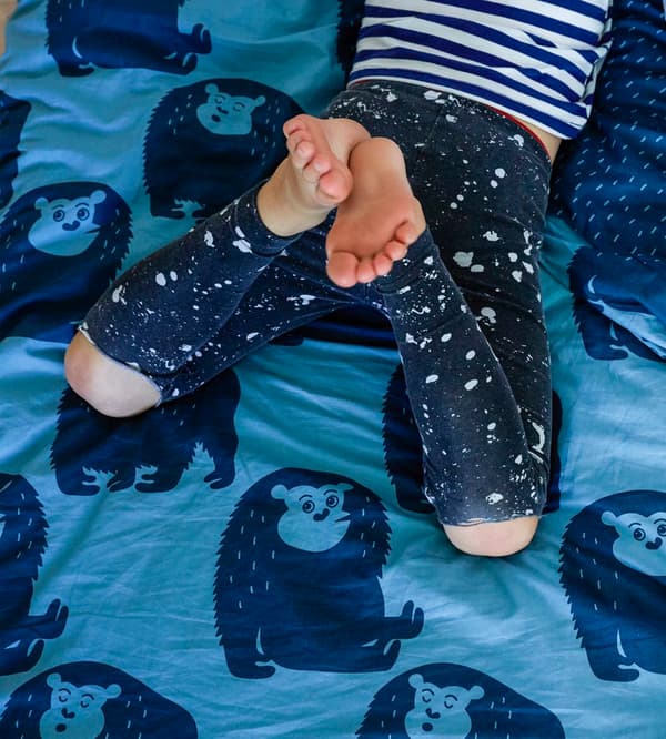As pernas dun neno que está sobre a cama con roupa de cama con estampado animal de cor azul.