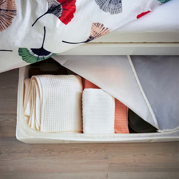 Asciugamani in una custodia a zip inserita sotto a un letto con biancheria a motivo floreale - IKEA