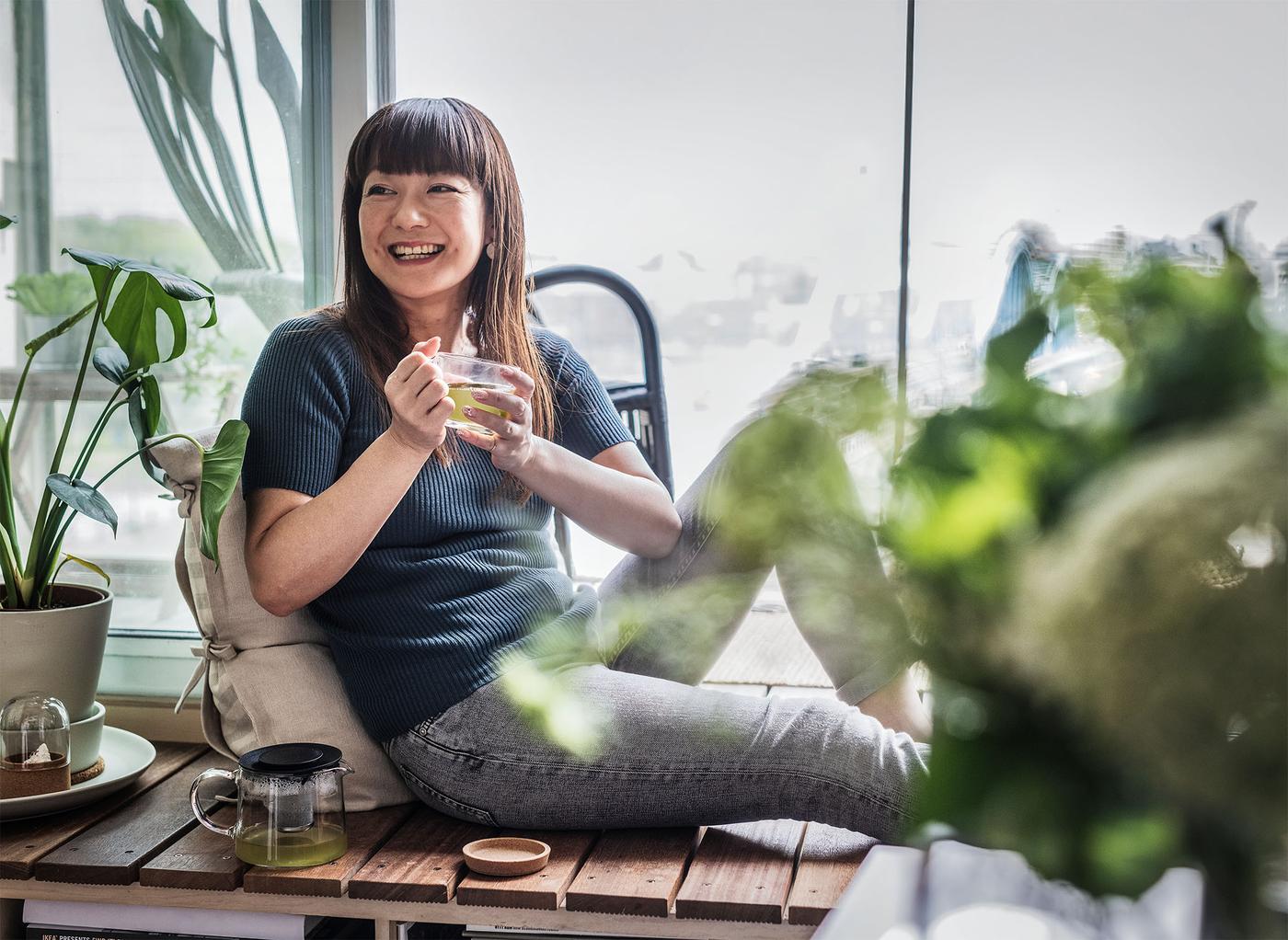 Asian woman holding a cup of tea and smiling to herself