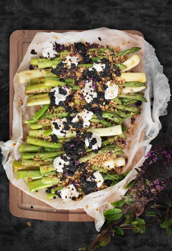 Asparagus salad with seaweed pearls and dollops of crème fraiche served on a wooden chopping board, seen from above.