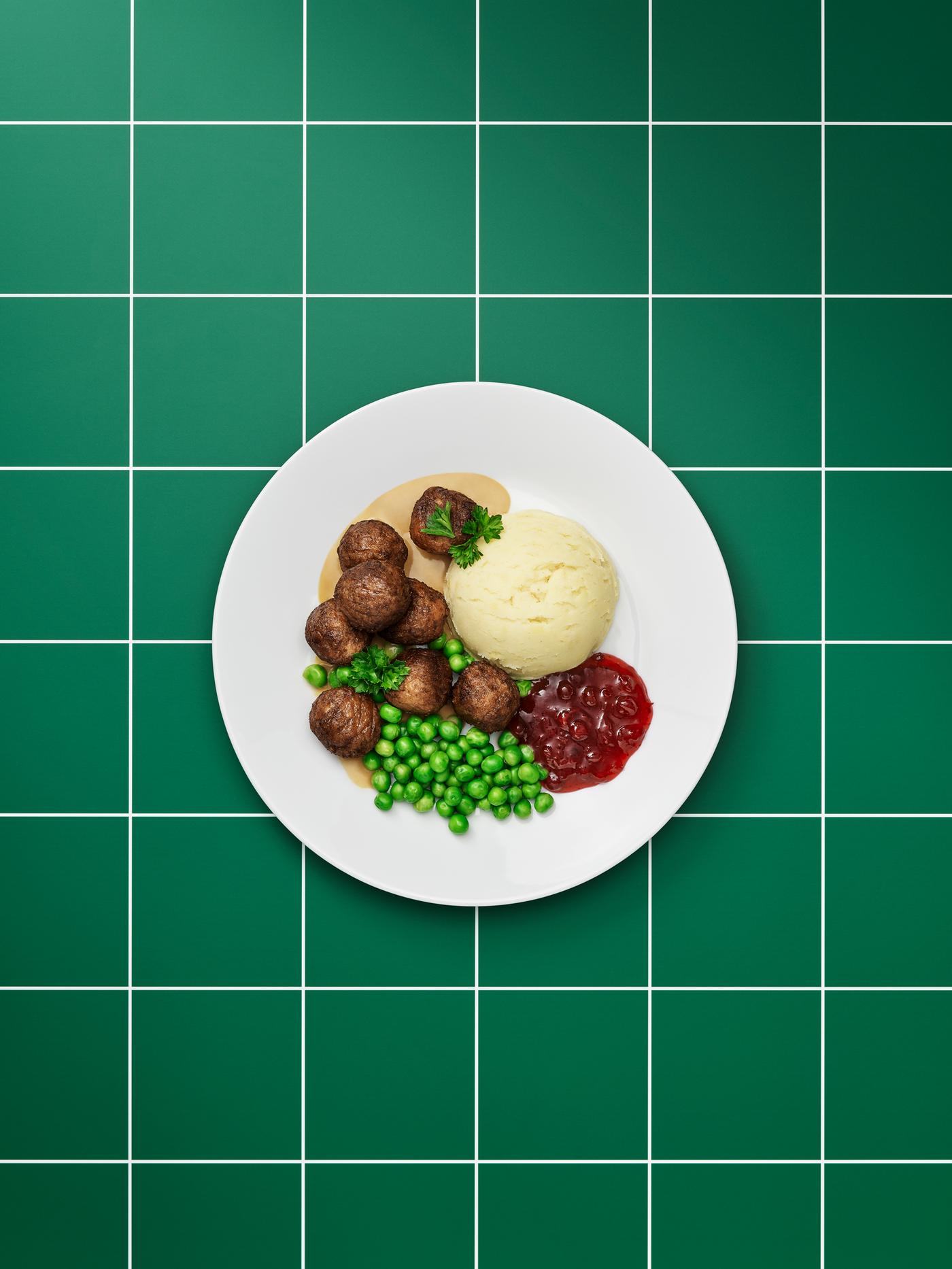 Assiette blanc uni contenant des boulettes végétales, de la sauce brune, de la purée, de la confiture d’airelles, des petits pois et un brin de persil.