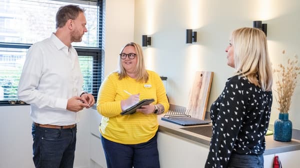Assise à un ordinateur portable, une collaboratrice IKEA portant une chemise jaune a en main trois échantillons de couleur dans des tons beige et ocre.