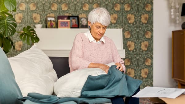 Assise sur un canapé, une femme portant un pull rose clair habille un coussin de canapé d’une housse bleue.