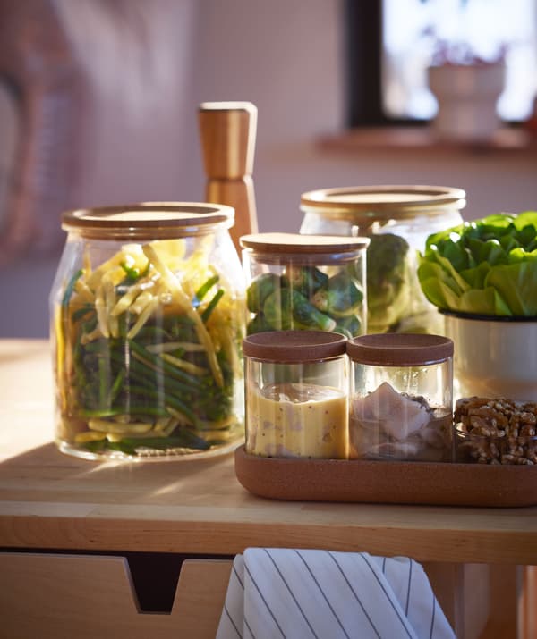 Assortiment de petits plats ou accompagnements – légumes, harengs, etc. – dans des bocaux de différentes tailles, placés sur une surface en bois.