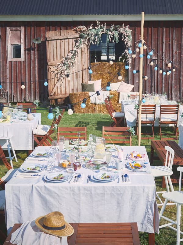 At an outdoor party, tables are set with GULLMAJ tablecloths, UPPLAGA plates, DYRGRIP glasses, and UPPHÖJD cutlery.