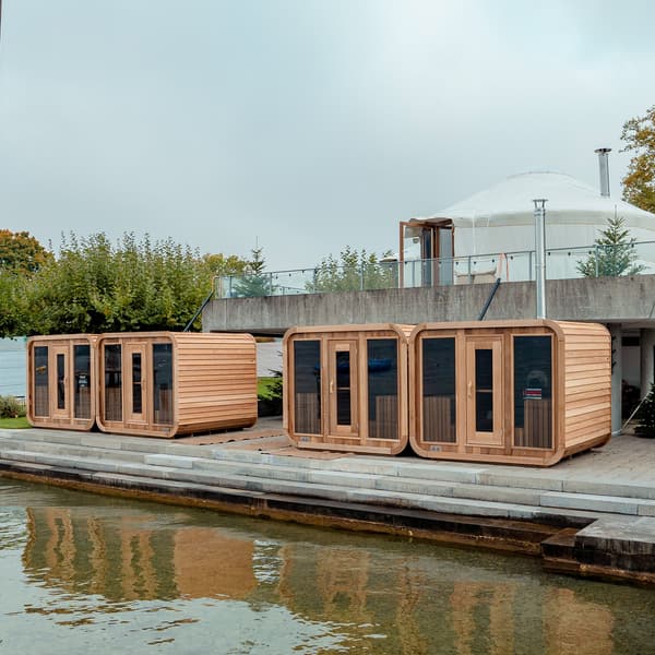 At the edge of a swimming pool are four wooden cubes, each with a sauna inside