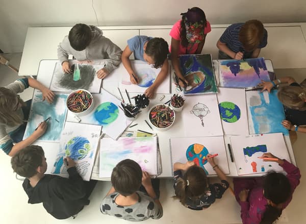 أطفال يجلسون حول طاولة ويرسمون صورًا للأرض.