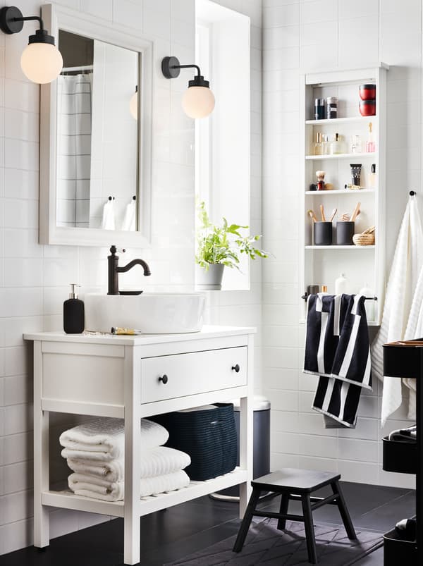 أثاث حمام HEMNES أبيض بدرج واحد ورف واحد مع مناشف وحنفية HAMNSKÄR ومرآة ومصباحين.