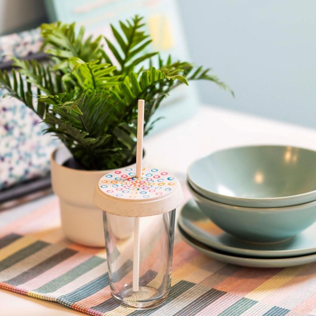 Auf diesem Bild sieht man eine Vase mit einer Pflanze auf dem Tisch. Daneben steht ein Glas und 2 Schüsseln und Teller in blau.