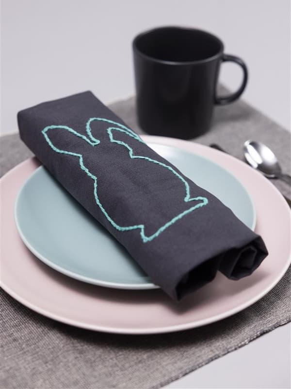 Auf einem blauen Teller liegt eine Serviette mit einem Hasen drauf und einer schwarzen Tasse oben rechts in der Ecke.