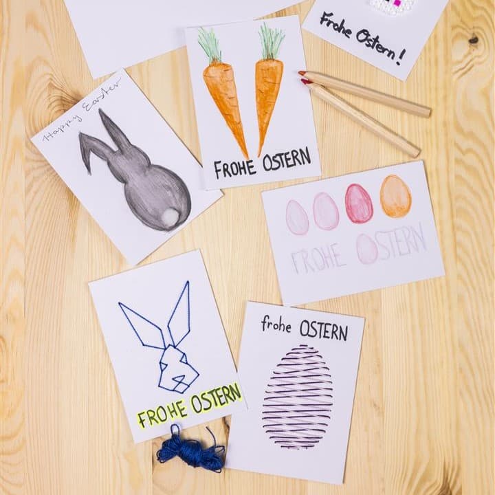 Auf einem Holztisch liegen Bilder von einem Osterhasen und Karotten