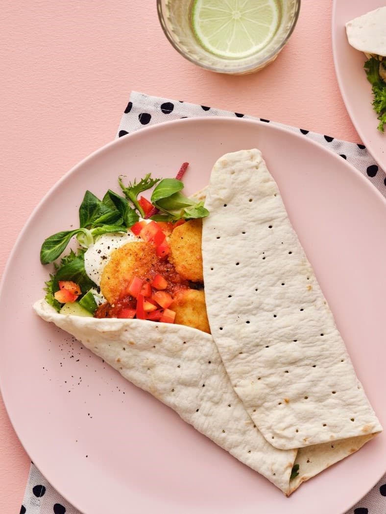 Auf einem pinken Teller liegt ein Wrap mit Gemüse darin.