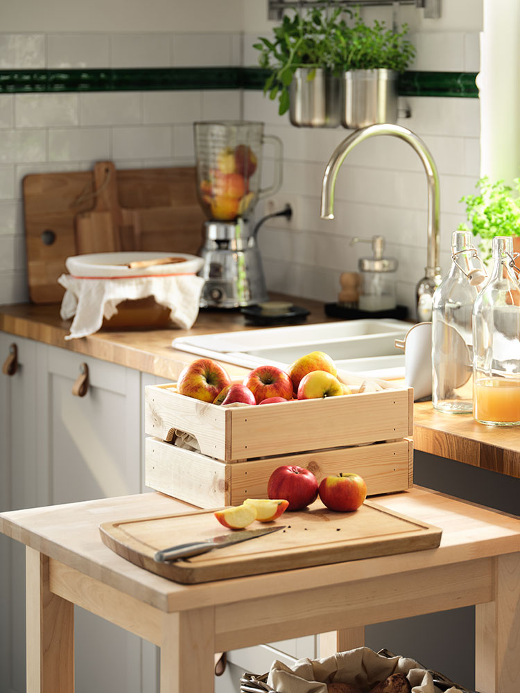 Auf einem Rollwagen aus Holz werden auf einem Schneidebrett Äpfel geschnitten und als Saft in Glasflaschen mit Verschluss gefüllt.