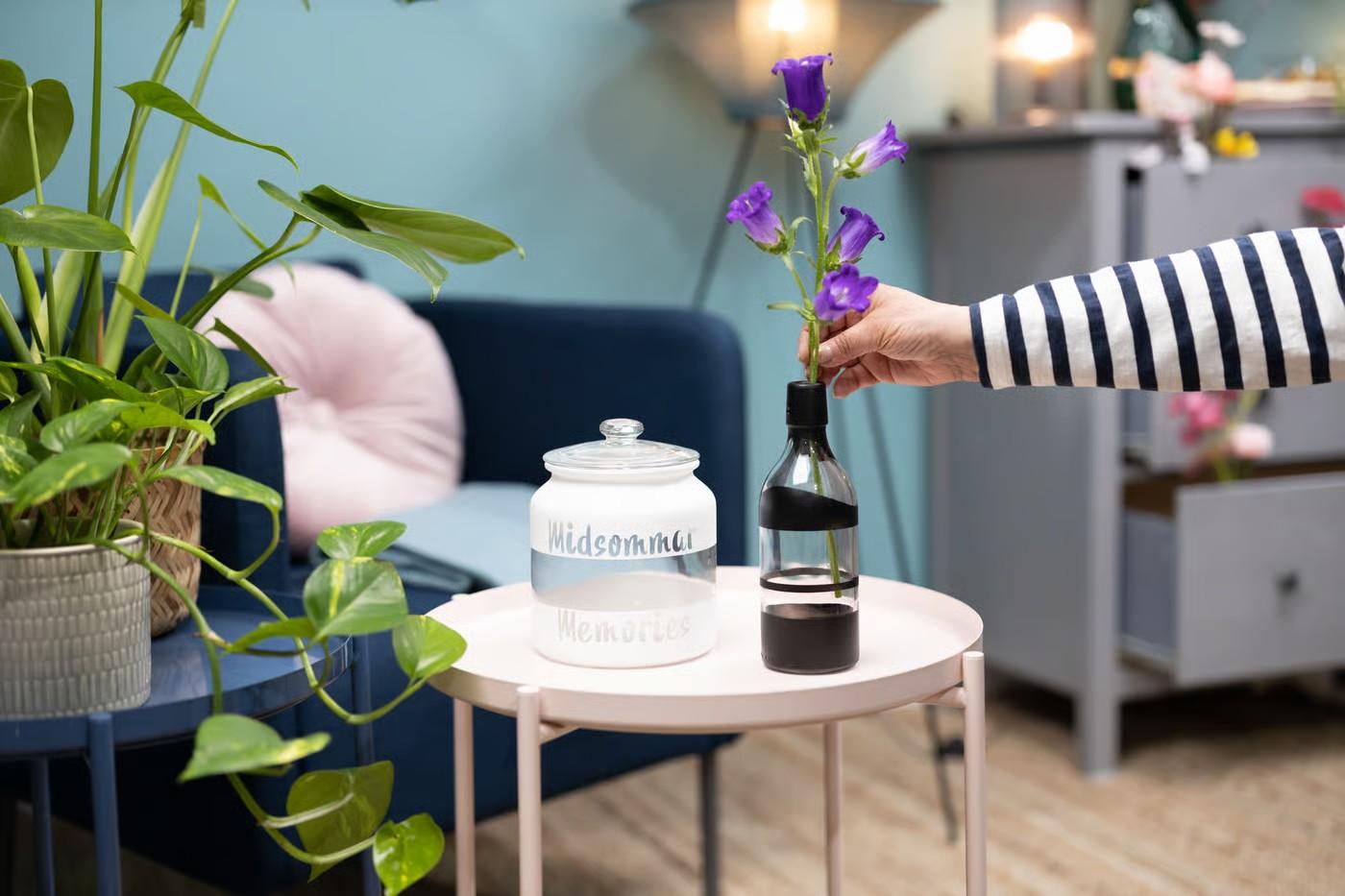 Auf einem rosanen Beistelltisch steht eine bemalte Glasvase und eine schwarze Vase mit lila Blumen.