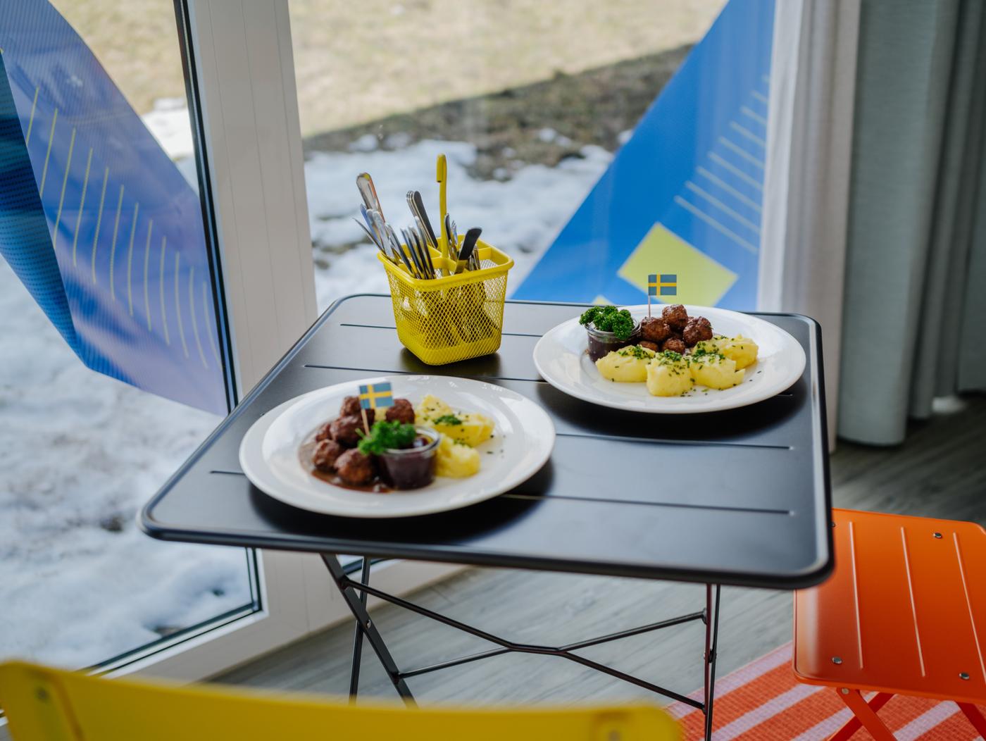 Auf einem schwarzen kleinen Tisch stehen 2 Teller mit Köttbullar und Kartofeln darauf und einem gelben Besteck behälter