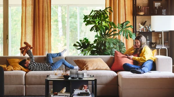 Auf einem Sofa sitzt rechts ein Mädchen mit einem Handy in der Hand und links spielt ein Junge mit einem Teddy.