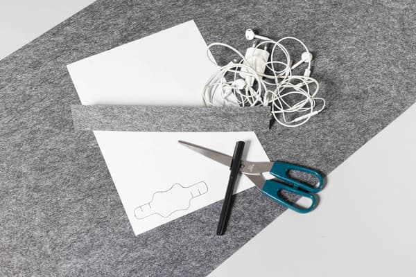 Auf einem Tisch liegt eine Schere eine graue Filzunterlage ein Papier für die Vorlage und ein dünner Filzstift. 