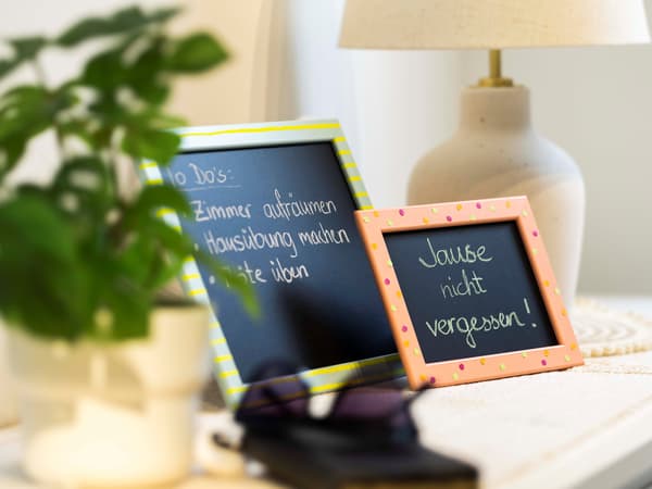 Auf einem Tisch neben einer Vase stehen 2 schwarze Tafeln mit einer Schrift darauf