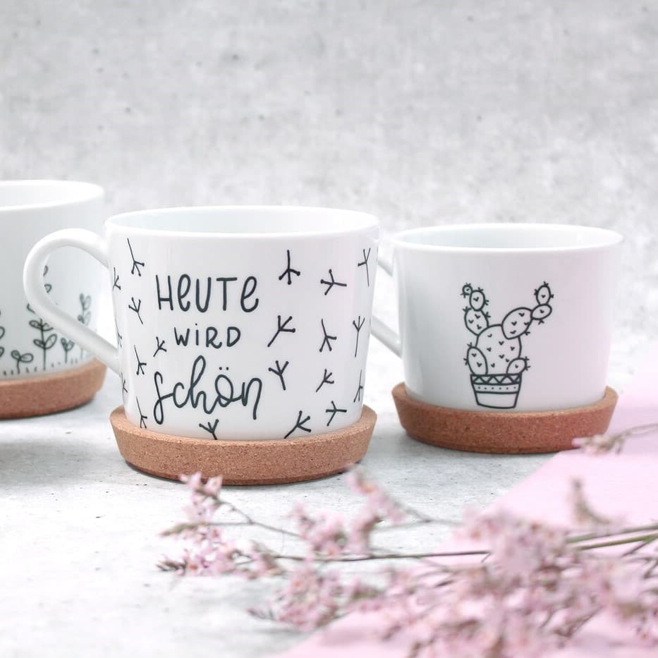 Auf einem Tisch stehen 3 Tassen mit einem Muster und einer Schrift darauf.