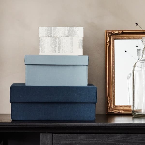 Auf einem Tisch stehen 3 verschiedene große Boxen in weiß und blau. Danben steht ein Bild und eine Vase.