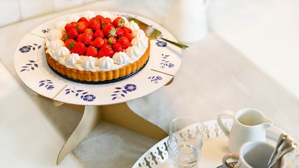 Auf einem Tisch steht ein selbstgemachter Tortenteller mit einer Erdbeer Torte darauf.