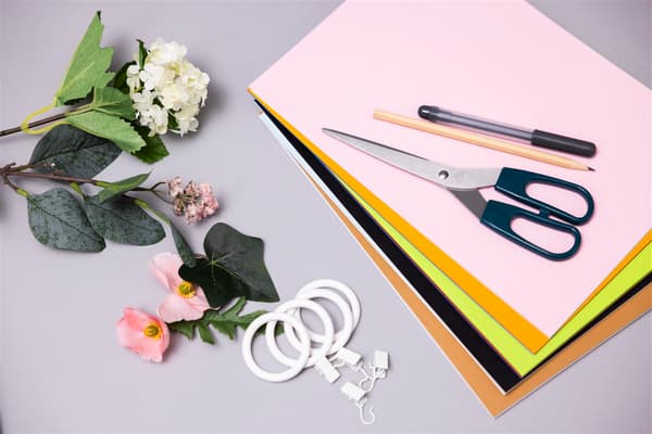 Auf einer hellen Oberfläche liegen Blumen und bunte Zettel mit einer Schere und einem Stift darauf.
