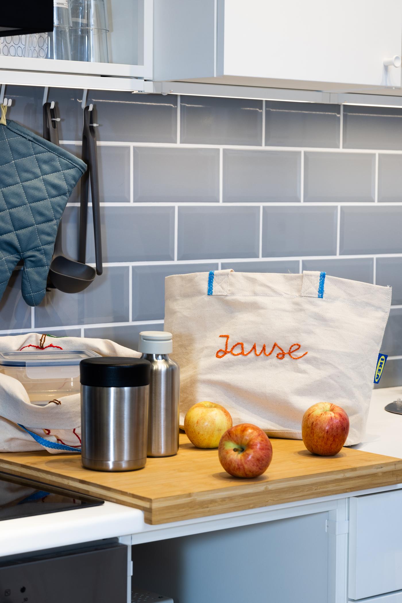 Auf einer Küchenplatte liegen 3 Äpfel und ein weißer Beutel mit der Schrift "Pause" darauf.