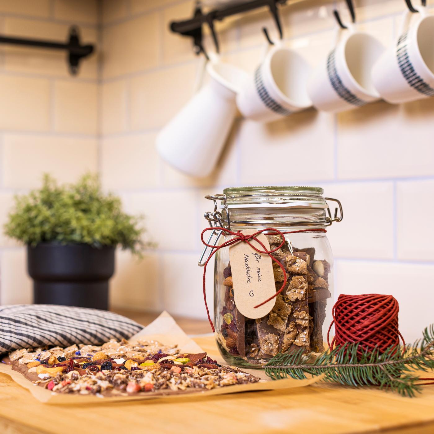 Auf einer Küchenplatte steht ein Glas mit Snacks darin. An der Wand hängt eine Stange mit Tassen daran.