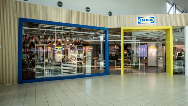 Außenansicht des IKEA Planungsstudios Dornbirn mit blauem und gelbem Eingangsrahmen, großen Glasfronten und einem einladenden Blick ins Innere des Studios.

