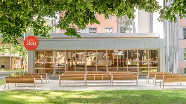 Außenansicht des Salon Stolz mit Bänken bei sonnigem Wetter.
