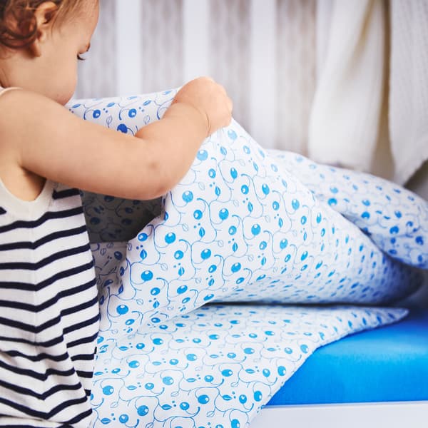 Bábätko drží posteľné obliečky GULSPARV zo 100 % bavlny so vzorom pripomínajúcim rastúce čučoriedky.