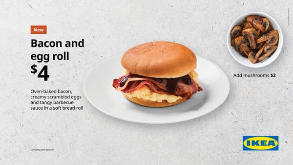 Bacon and egg roll. White plate on concrete background with white bread bun with egg and bacon inside. With a small bowl of mushrooms off to the side for an extra $2. Total price is $4