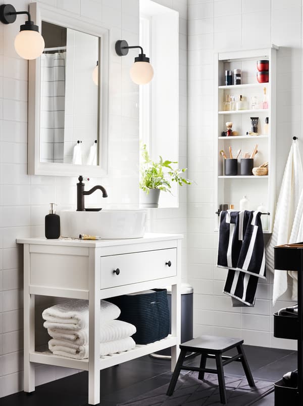 Bagno con mobile per lavabo con un cassetto e scaffale da parete HEMNES bianchi, asciugamani, miscelatore HAMNSKÄR, specchio e due lampade.