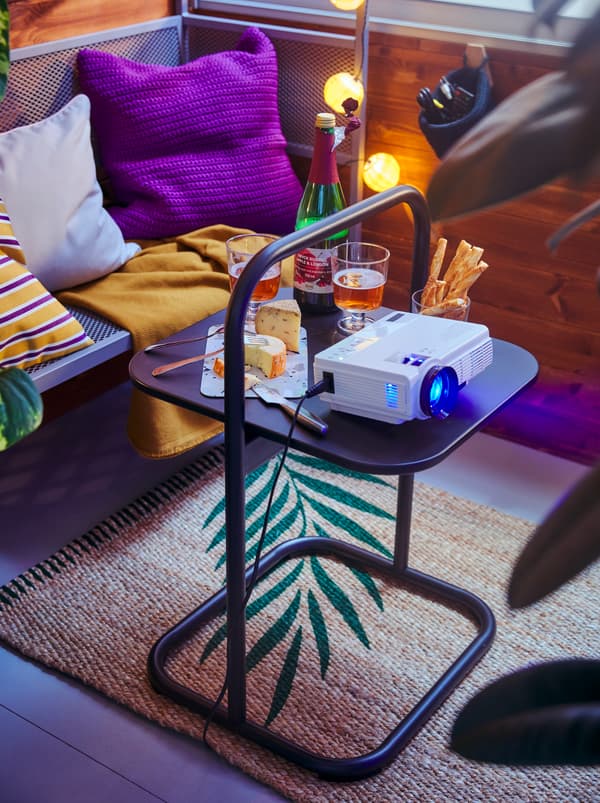 Bahagian balkoni yang mempunyai snek, minuman dan projektor filem kecil di atas meja sisi HUSARÖ dekat dengan bangku panjang arbor SVANÖ yang terdapat kusyen.