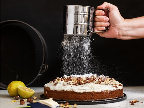 Baker uses rubber spatula to frost a cake on glass cake stand