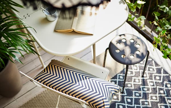 Balcon vu d’en haut avec tasse de café et livre sur une table, deux sièges et deux tapis par terre.