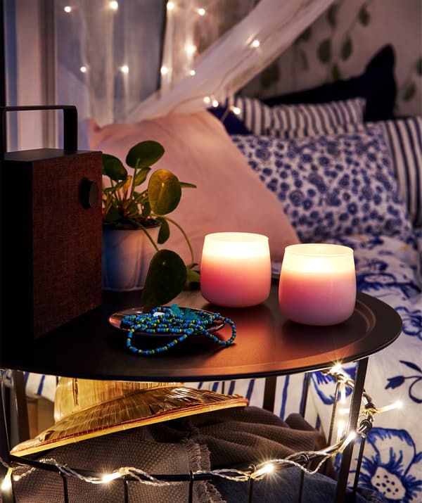 Balcone con un letto, un tavolino rotondo, una cassa bluetooth ENEBY e delle candele profumate accese - IKEA