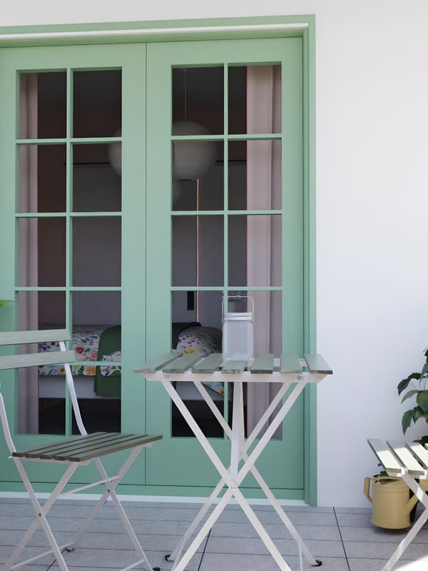 Balcony with table and two chairs and green door behind.