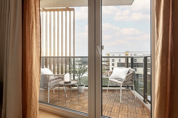 Balcony with wooden deck flooring, outdoor chairs, and table with lamp.