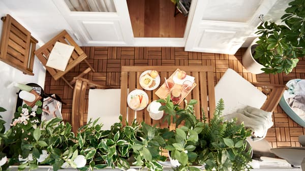 Balkon koji karakterišu letvice od bagremovine – NÄMMARÖ nameštaj i RUNNEN podne obloge – i lisnata FEJKA veštačka biljka.