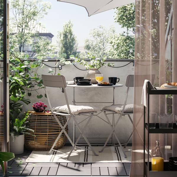 Balkon s sivo SUNDSÖ zunanjo mizo in dva siva zunanja stola na preprogi ter klubska mizica, rastline in senčnik.