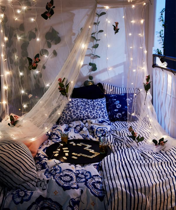 Balkón v noci s dvojmiestnou posteľou, podnosom s nápojmi a sieťou so svetelnými reťazami LED IKEA LEDFYR.