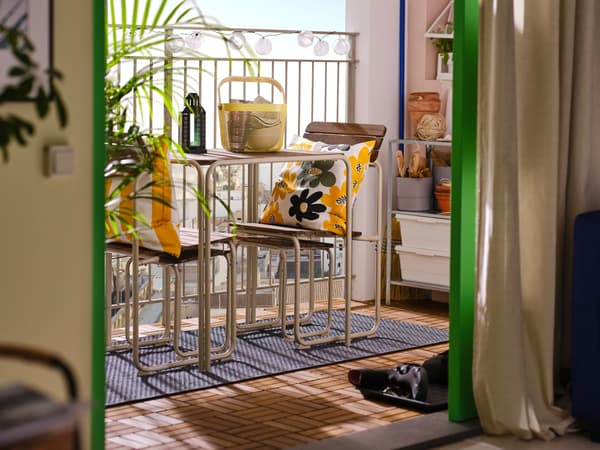 Balkon widziany z pokoju dziennego, a na nim: stół FURUÖN z 2 krzesłami i 2 podnóżkami oraz kolorowe poduszki.