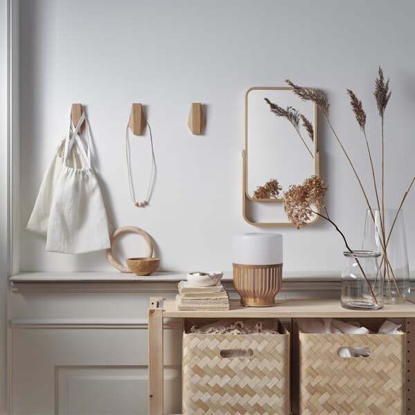 Bamboo storage boxes in a wooden unit, a mirror and wooden hooks on a white wall.