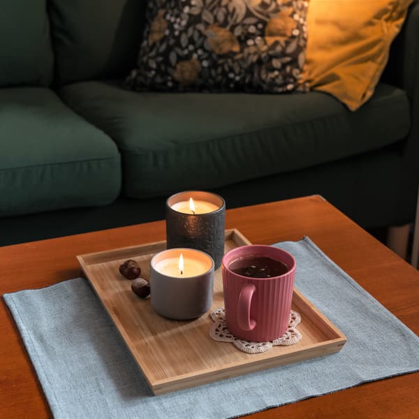 Bambusowa taca OSTBIT, na której stoja świece zapachowe i kubek herbaty.