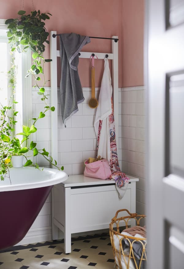 Banc de rangement avec barre porte-serviettes HEMNES dans le coin d'une salle de bain aux murs rose pâle et blanc