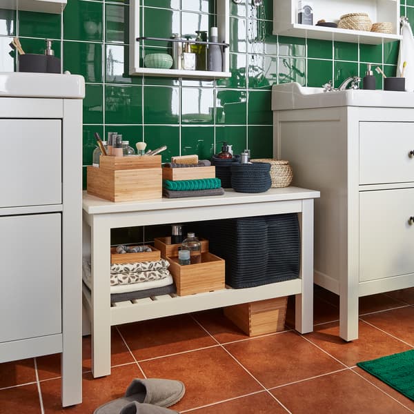 Banc HEMNES blanc entre deux meubles-lavabos. Boîtes et serviettes rangées sur les tablettes du banc.
