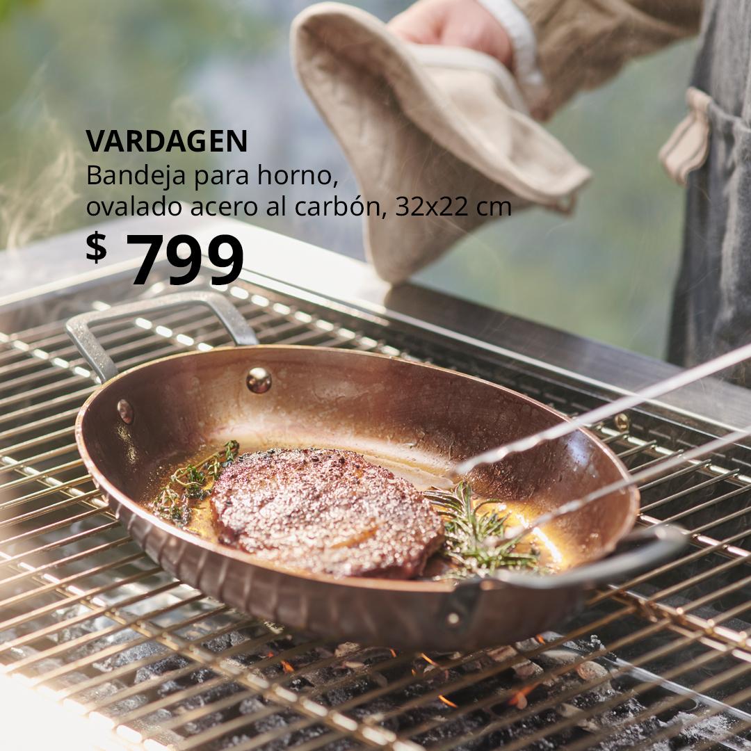 Bandeja para horno VARDAGEN de cobre sobre parrilla exterior, carne dorada con romero y tomillo en mantequilla, vapor visible y pinzas metálicas; utensilio resistente ideal para cocina al aire libre.